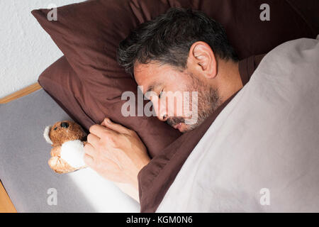 Hohe Betrachtungswinkel von reifer Mann schlafen von kleinen Teddybär auf dem Bett zu Hause. Stockfoto