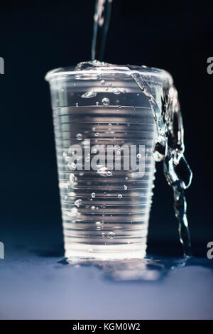 In der Nähe von Wasser im Überquellenden Glas auf dem Tisch auf schwarzem Hintergrund gießen Stockfoto
