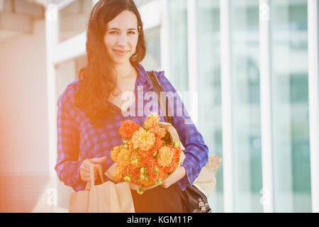 Portrait von lächelnden Frau mit Blumenstrauß stehend gegen Gebäude Stockfoto