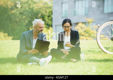Kollegen diskutieren beim Sitzen auf Gras Feld Stockfoto