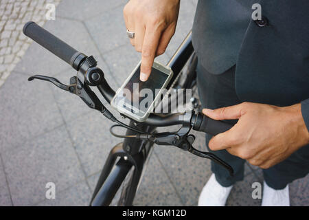 Untere Partie der Geschäftsmann mit Smart Phone auf dem Fahrrad Griff beim Stehen auf der Straße Stockfoto