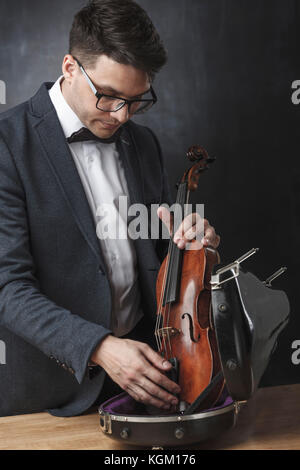 Junger Mann, der Violine im Falle am Tisch auf schwarzem Hintergrund Stockfoto