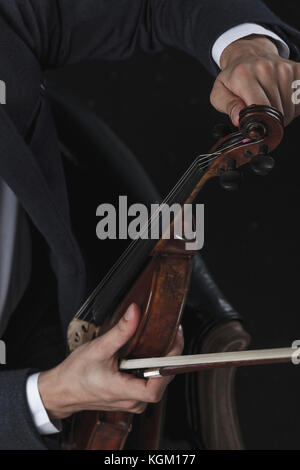 Zugeschnittenes Bild von geiger tuning Violine sitzend auf Stuhl Stockfoto