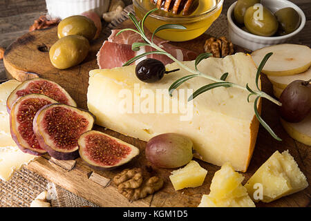 Käseplatte mit verschimmelten Käse, Schinken, eingelegten Pflaumen, Oliven, Trauben, Feigen, Honig, Nüssen auf alten Holz- Hintergrund. Im rustikalen Stil. Stockfoto