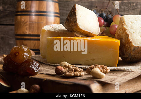 Die Zusammensetzung von Lebensmitteln mit Bausteinen von verschimmelten Käse, getrocknet Datteln, Trauben, Oliven, Feigen auf alten Holz- Hintergrund. Stockfoto