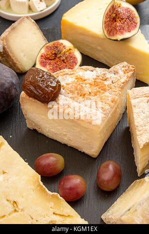 Die Zusammensetzung von Lebensmitteln mit Bausteinen von verschimmelten Käse, Trauben, Feigen auf schwarzen Hintergrund. Stockfoto