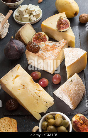 Die Zusammensetzung von Lebensmitteln mit Bausteinen von verschimmelten Käse, eingelegte Pflaumen, Weintrauben, Oliven, Feigen, Cracker, Feigen auf schwarzen Hintergrund. Stockfoto