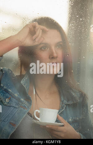 Nachdenklich schöne Frau mit Tasse Kaffee, während Sie durch das Fenster Stockfoto