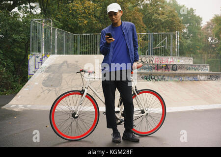 Volle Länge des Menschen mit Mobiltelefon, während sie mit dem Fahrrad in PARK-Stellung Stockfoto