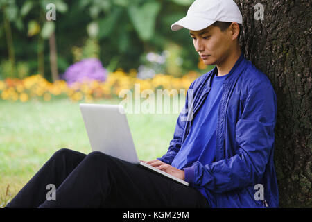 Junger Mann mit Laptop, während Sie von Baum im Park sitzen Stockfoto