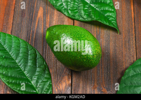 Eine grüne Reif rohe avocado Obst mit Blättern liegt auf einer hölzernen braun Tabelle. top View Stockfoto