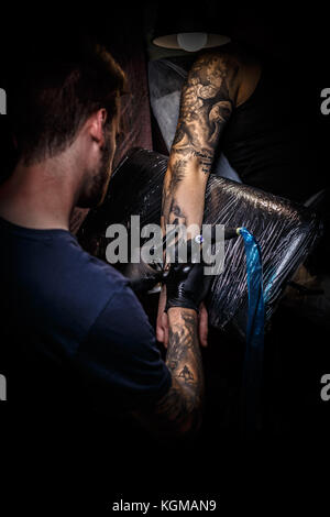 Master tattoo zieht die schwarze Farbe auf den Clients tattoo. Stockfoto