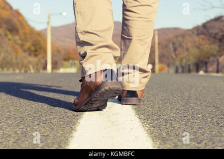 Rückansicht der männlichen Füße gehen und tragen im Herbst real oder echtem Leder Schuhe in der Mitte der eine asphaltierte Straße an einem sonnigen Herbst Tag Stockfoto