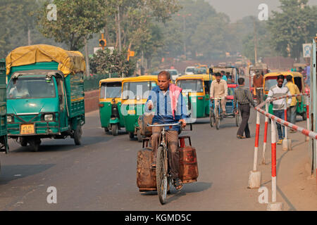 Delhi, Indien - 20. November 2015: Mann auf einem Fahrrad in der gedrängten Verkehr mit bunten Tuk-tuk Fahrzeuge und sichtbare smog Luftverschmutzung Stockfoto