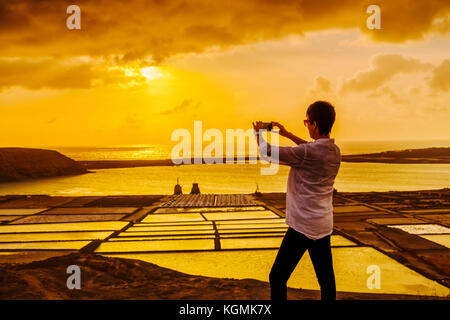 Salze. Frau, die bei Sonnenuntergang in Salinas de Janubio fotografiert. Lanzarote Island. Kanarische Inseln Spanien. Europa Stockfoto