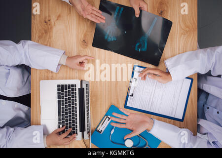 Ärzte diskutieren X-rays am Schreibtisch. Ärzte weisen auf die medizinische Geschichte. Konzept von Medizin und Gesundheitswesen Stockfoto