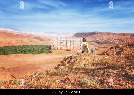 Junge Frau von befestigte Stadt suchen. Glaoui Kasbah von Telouet Kasbah oder Ksar in Marokko Blick von oben. Reisende Mädchen sitzt auf einem Felsen schaut auf das Tal von Ounilla Stockfoto