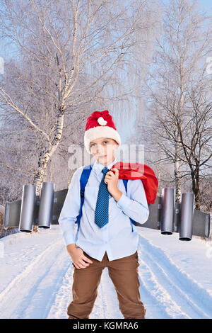 Junge Santa Claus mit einem Jetpack auf dem Rücken hält Geschenke für Weihnachten auf Winter Holz Straße Stockfoto