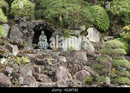 Bonsai Bäume wachsen im Freien in einem Garten am Hang mit einer Statue in einer kleinen Höhle sitzend, Naritasan Tempel, Narita, Japan, 16. April 2012 Stockfoto