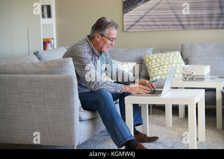 Älterer Mann im Wohnzimmer mit Laptop Stockfoto