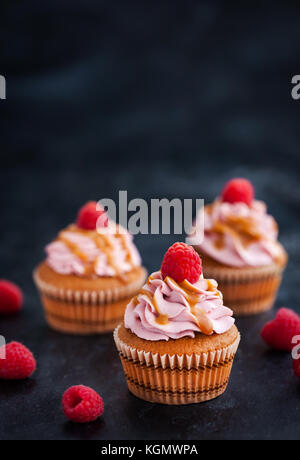 Leckere Himbeeren und Karamell Cupcakes auf dunklem Hintergrund Stockfoto
