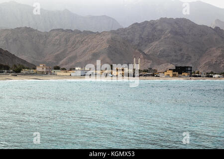 Blick auf einen leeren Strand in Oman mit Moschee und traditioneller arabischer Architektur, al Hajar Berge im Hintergrund Stockfoto