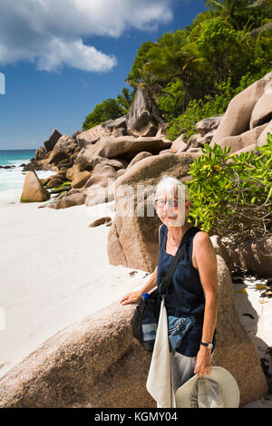 Die Seychellen, La Digue, Petit Anse, Senior Frau touristische unter Granit Felsen am Strand Stockfoto