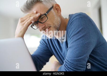 Mann zu Hause in Kopfschmerzen vor Laptop Stockfoto