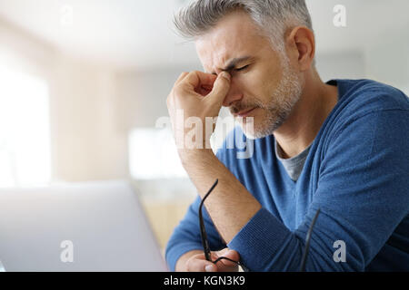 Mann zu Hause in Kopfschmerzen vor Laptop Stockfoto