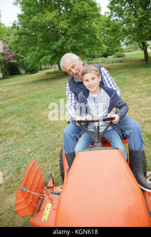 Älterer Mann mit grandkid Reiten auf Rasenmäher Stockfoto