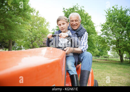 Älterer Mann mit grandkid Reiten auf Rasenmäher Stockfoto