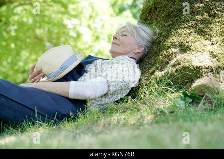 Ältere Frau entspannen im Garten durch Baum Stockfoto