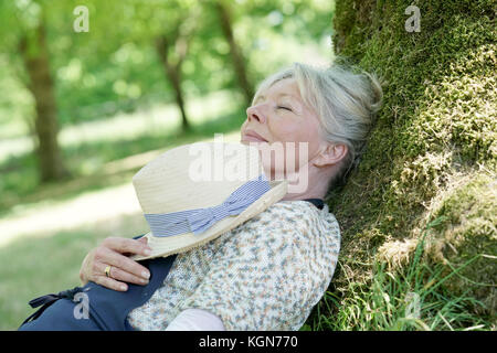 Ältere Frau entspannen im Garten durch Baum Stockfoto