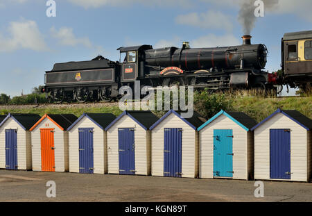 Dampfzug vorbei Holzhütten Am Goodrington Sands, geschleppt von GWR Lok Nr.7827 Lydham Manor. Stockfoto