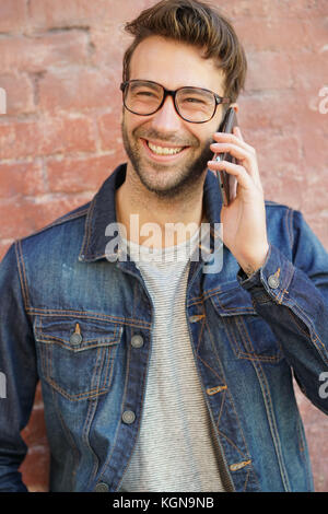Lächelnd trendy Kerl mit Brille durch die Mauer steht am Telefon sprechen Stockfoto