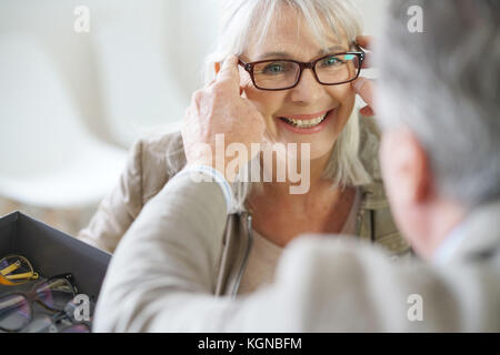 Ältere Frau in optischen Speichern versuchen, Brillen auf Stockfoto