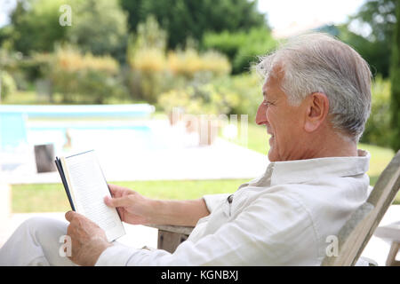 Älterer mann Lesung buchen Sie im Pool deck Chair Stockfoto