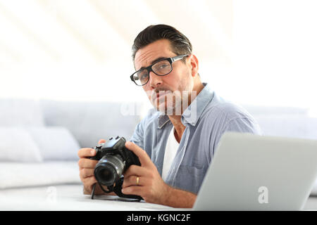 Mann an mit Spiegelreflexkamera home und Laptop Stockfoto