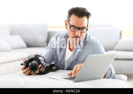 Mann an mit Spiegelreflexkamera home und Laptop Stockfoto