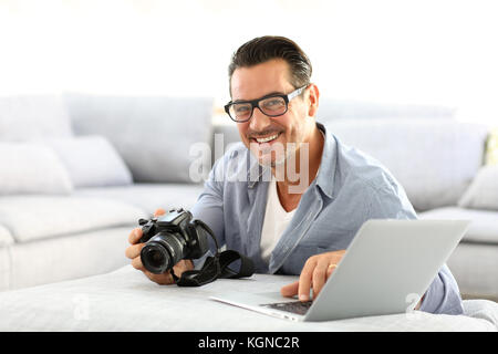 Mann an mit Spiegelreflexkamera home und Laptop Stockfoto