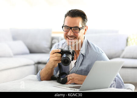 Mann an mit Spiegelreflexkamera home und Laptop Stockfoto