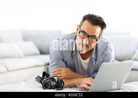 Mann an mit Spiegelreflexkamera home und Laptop Stockfoto
