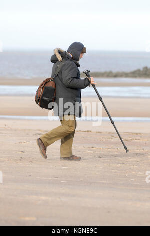 New Brighton Wirral, 9. November 2017. uk Wetter. windig, schauerwetter über aus dem Westen heute einen hellen Nachmittag zu verlassen, sondern mit zunehmender Wind. ein Fotograf auf den Weg zum Strand wie der treibsand Peitsche und gekleidet für den kalten und windigen Bedingungen in New Brighton Stockfoto