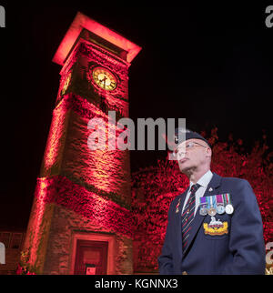 Nailsworth, Gloucestershire, Großbritannien, 10. November 2017. Der ehemalige Soldat Desmond Cox, der in der Grafschaft Gloucestershire Regiment gedient, dargestellt durch die Clock Tower im Zentrum von Nailsworth, die mit Mohn eingerichtet wurde und in rot beleuchtet, vor Der Armistice Day und Erinnerung Sonntag. Credit: Gavin Crilly/Alamy leben Nachrichten Stockfoto