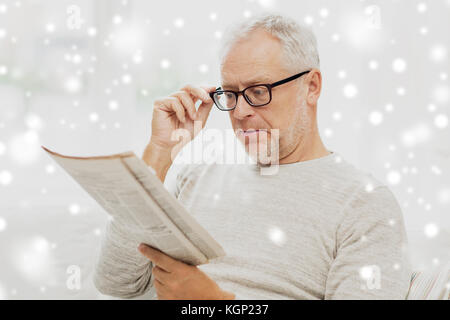 Älterer Mann in der Brille lesen Zeitung über Schnee Stockfoto