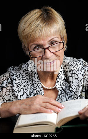 Portrait von eine ältere Frau mit einem Buch in Gläsern auf schwarzem Hintergrund Stockfoto