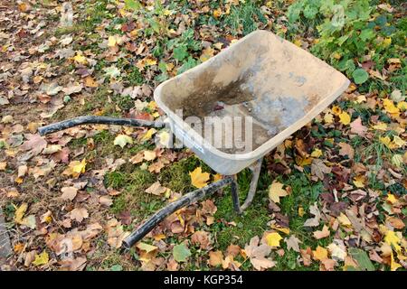 Leeren alten Erbauer Schubkarre im Herbst Garten auf Blatt übersäten Rasen. Stockfoto