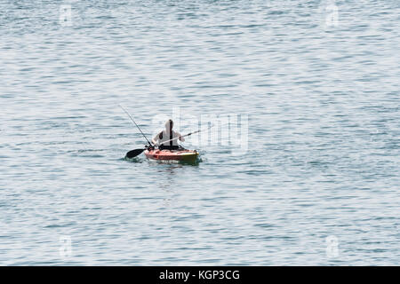 Einsame Meer angler paddeln Kajak gegen das Wasser. Die Fischerei auf Makrele in flachen Gewässern in der Nähe von Par, Cornwall. Isolation Konzept. Stockfoto