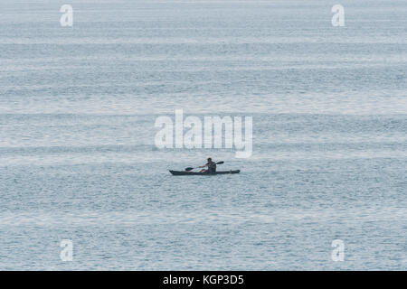 Einsame Meer angler paddeln Kajak gegen das Wasser. Die Fischerei auf Makrele in flachen Gewässern in der Nähe von Par, Cornwall. Isolation Konzept. Stockfoto