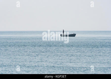 Fernen Schuss von Silhouette von Lone Fischer handlining von der Rückseite der Boot in Cornwall. Allegorie für Phishing, Katastrophenvorsorge, Isolation Konzept Stockfoto